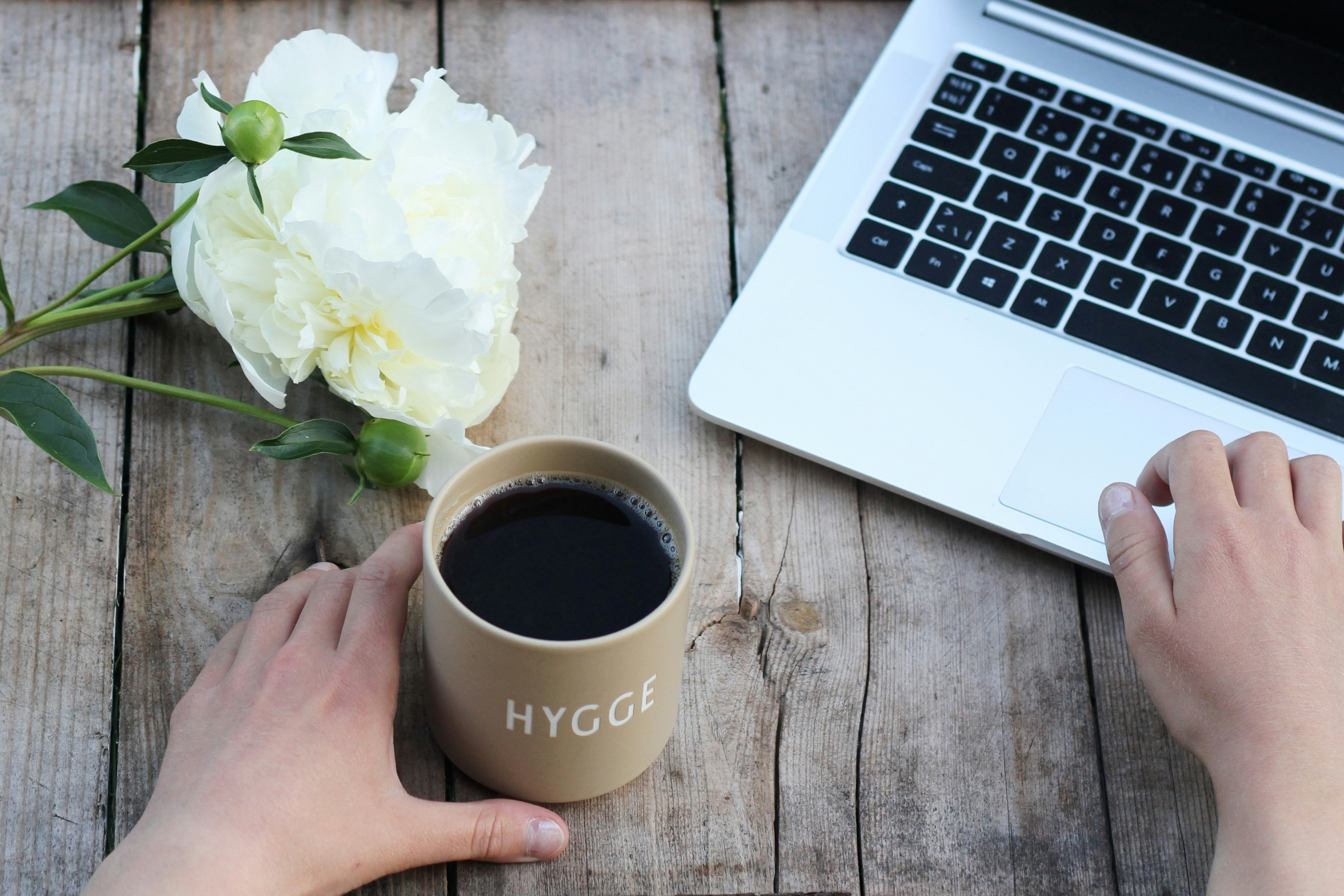 Une tasse de café sur une table en bois accompagnée d'une fleur blanche et d'un ordinateur portable.